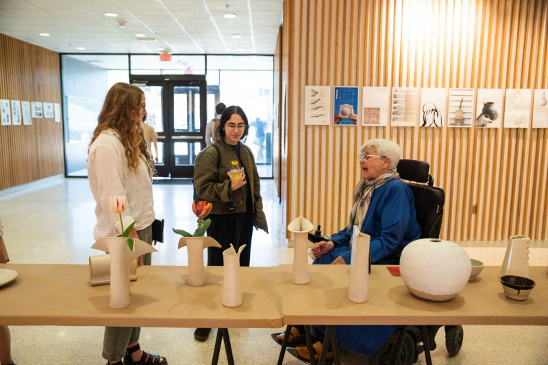 Ellen Braaten talks with two students in Cowgill lobby about ceramics displayed on table